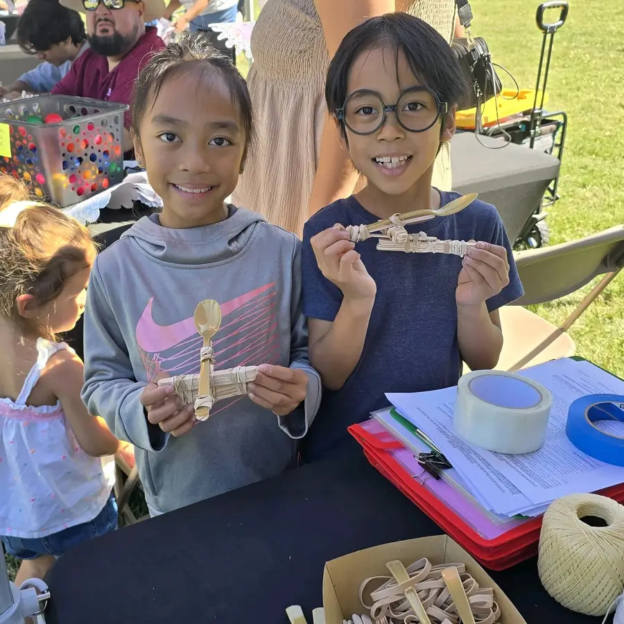 Two kids hold up popsicle-stick catapults they built at a STEM table