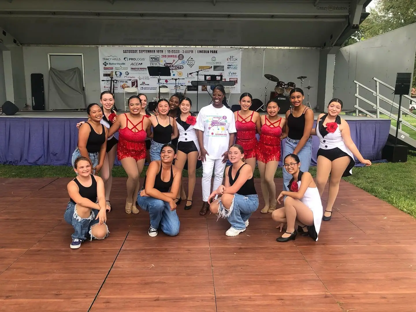 A youth dance team poses on the Tracy Connects stage in front of the sponsor banner
