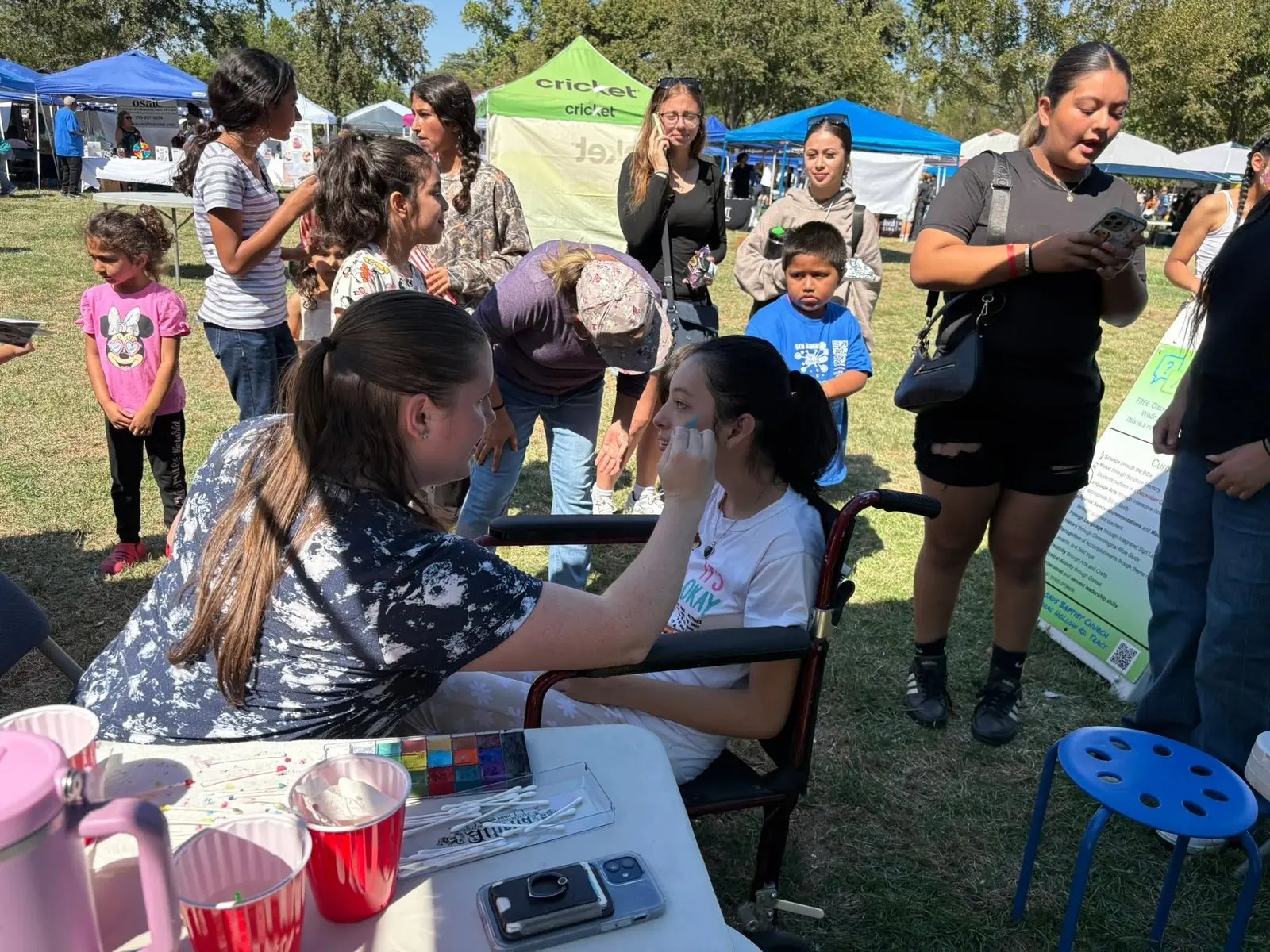 A volunteer face painter works while kids and families wait their turn at Tracy Connects