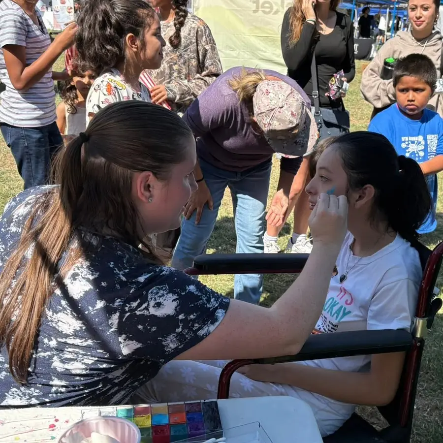 A volunteer paints a design on a young girl's cheek at Tracy Connects