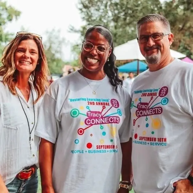 Three volunteers in 2022 Tracy Connects shirts smiling at the event