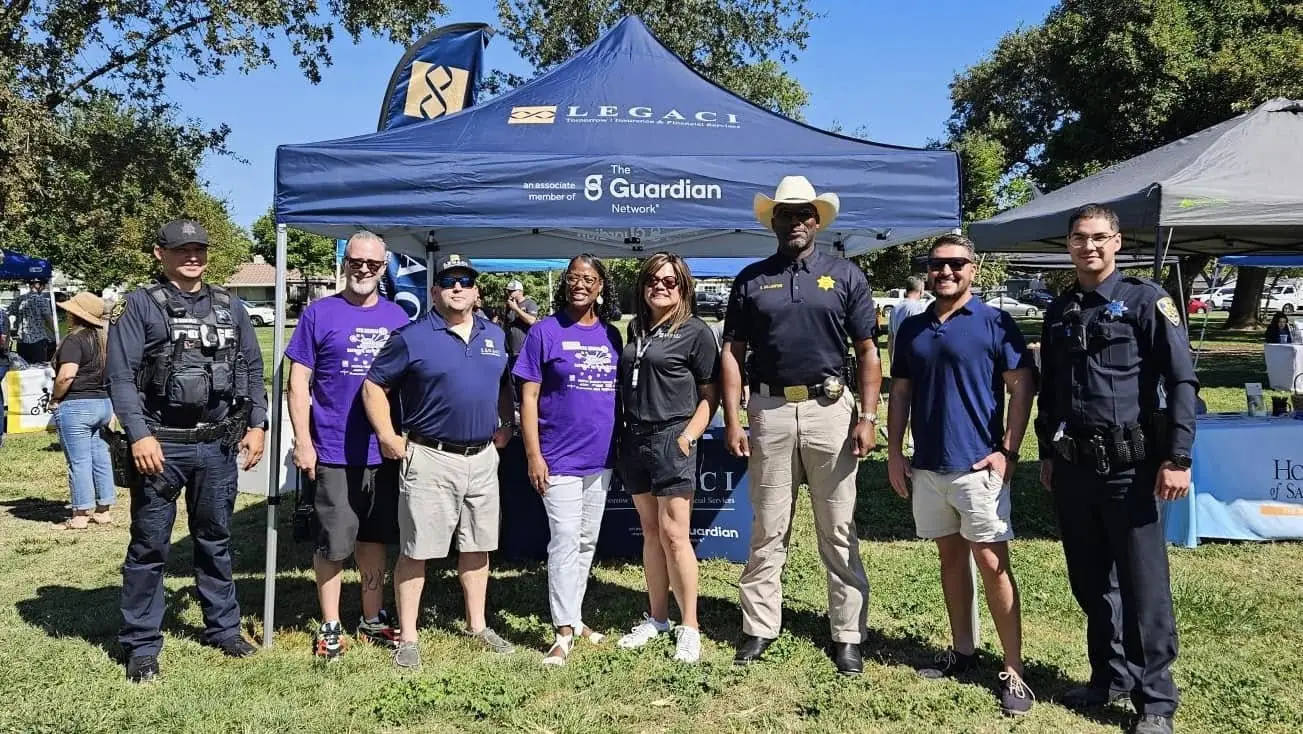 Police officers, a sheriff's deputy, and local business owners pose in front of a sponsor tent at Tracy Connects