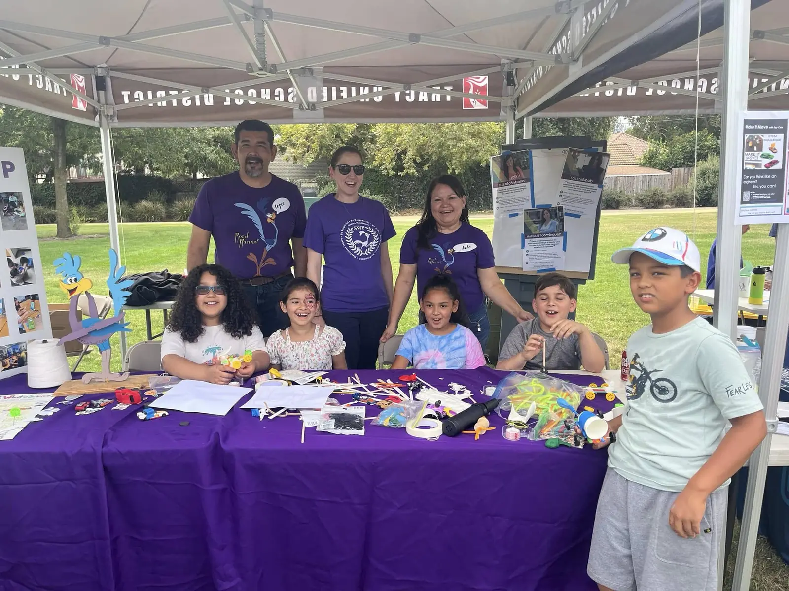 Kids laughing while building small cars at the Tracy Unified STEM tent, with teachers behind them